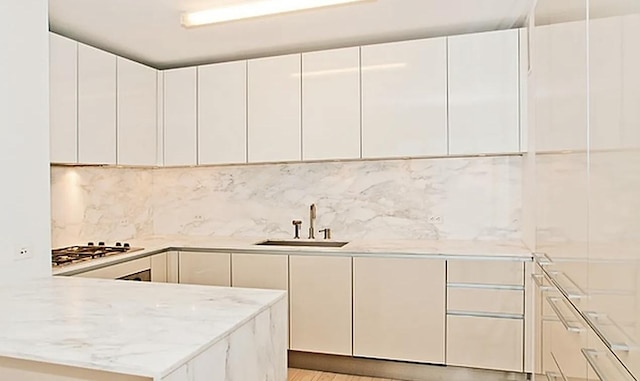 kitchen with a sink, gas cooktop, white cabinetry, a peninsula, and light stone countertops