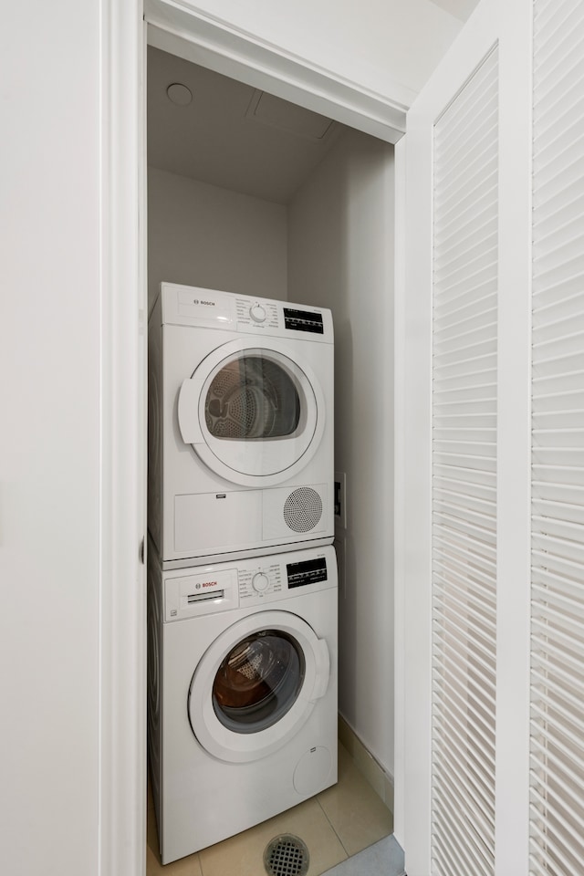 clothes washing area featuring tile patterned flooring, laundry area, and stacked washing maching and dryer