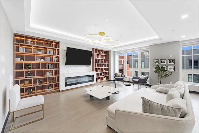 living room featuring wood finished floors, a raised ceiling, built in features, and a glass covered fireplace