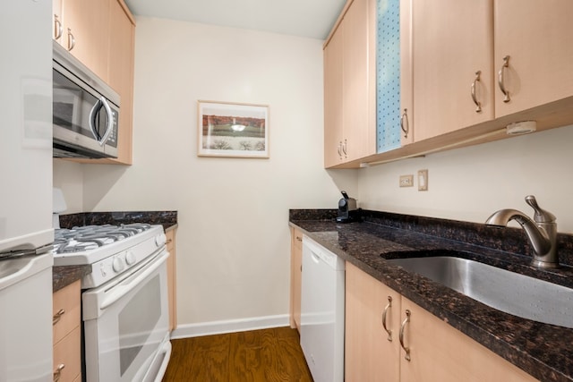 kitchen featuring dark wood-type flooring, light brown cabinetry, a sink, dark stone counters, and white appliances