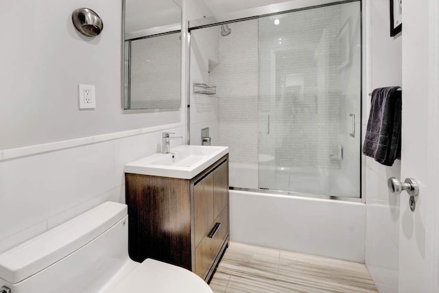 full bath with toilet, vanity, wainscoting, combined bath / shower with glass door, and tile walls