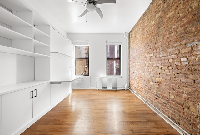 unfurnished room featuring radiator heating unit, wood finished floors, brick wall, and ceiling fan