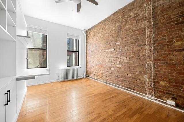 empty room with brick wall, baseboards, ceiling fan, radiator heating unit, and hardwood / wood-style floors