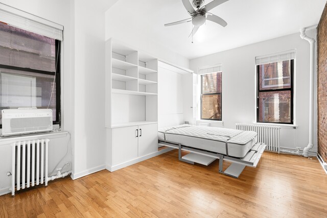 unfurnished bedroom with cooling unit, baseboards, light wood-style floors, and radiator heating unit