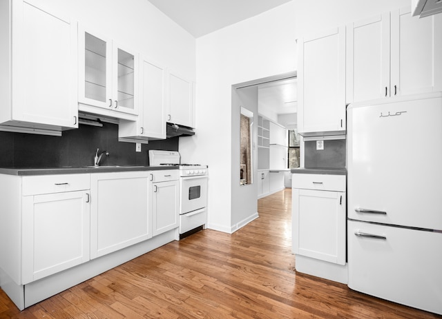 kitchen with dark countertops, under cabinet range hood, light wood-style floors, white cabinets, and white appliances