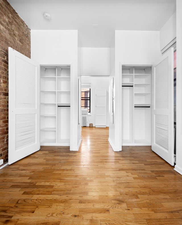 unfurnished bedroom with radiator, brick wall, multiple closets, and light wood finished floors