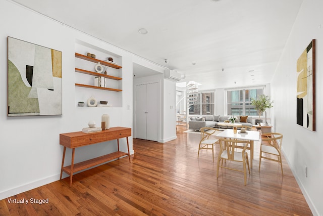 dining space featuring stairs, a wall unit AC, wood finished floors, and baseboards