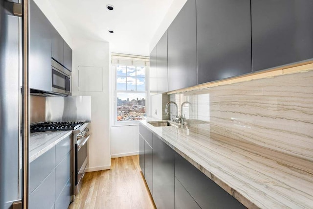 kitchen with light stone counters, a sink, decorative backsplash, stainless steel appliances, and modern cabinets