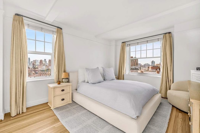 bedroom featuring baseboards, light wood-style flooring, and a view of city