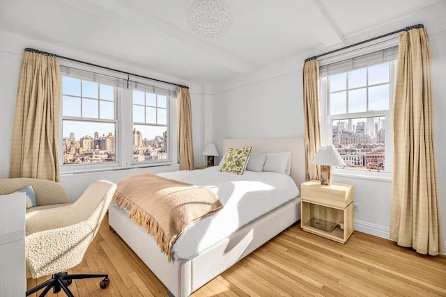 bedroom with beam ceiling, a view of city, light wood-type flooring, and baseboards