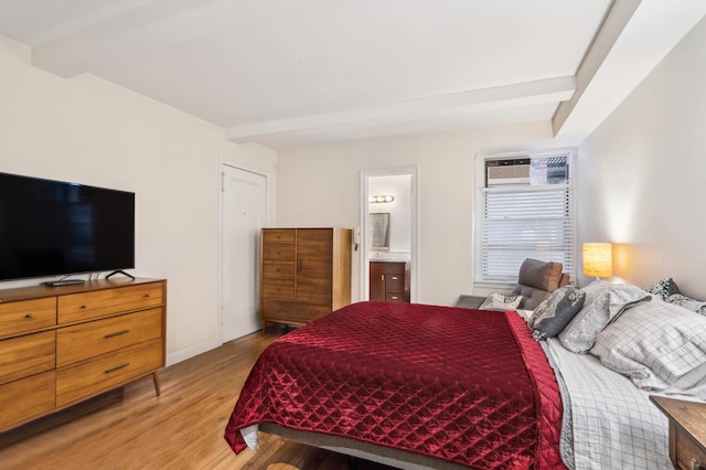 bedroom featuring light wood-type flooring, beam ceiling, and ensuite bathroom