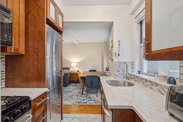 kitchen featuring a sink, stainless steel appliances, light stone counters, and decorative backsplash