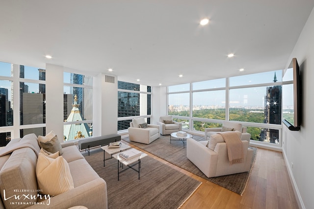 living area featuring light wood finished floors, visible vents, baseboards, a wall of windows, and recessed lighting