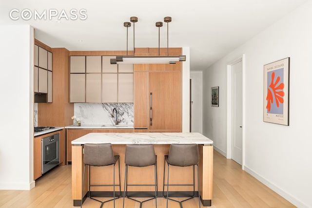 kitchen with light wood finished floors, a breakfast bar, a sink, stainless steel gas stovetop, and tasteful backsplash