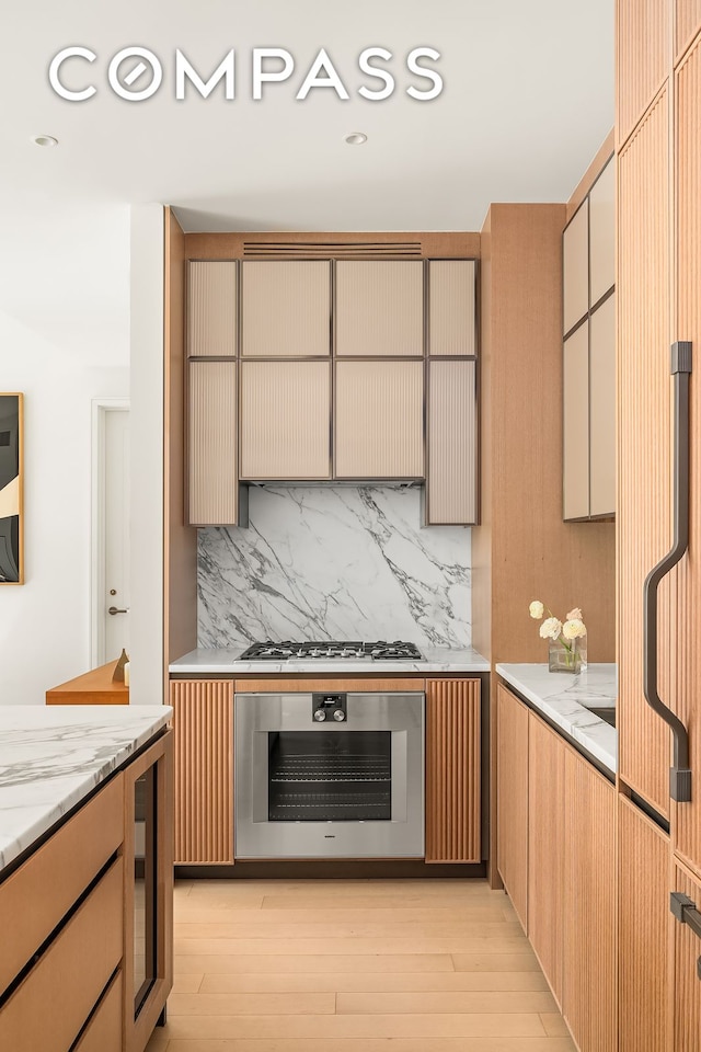 kitchen with light stone counters, backsplash, recessed lighting, light wood-style floors, and appliances with stainless steel finishes