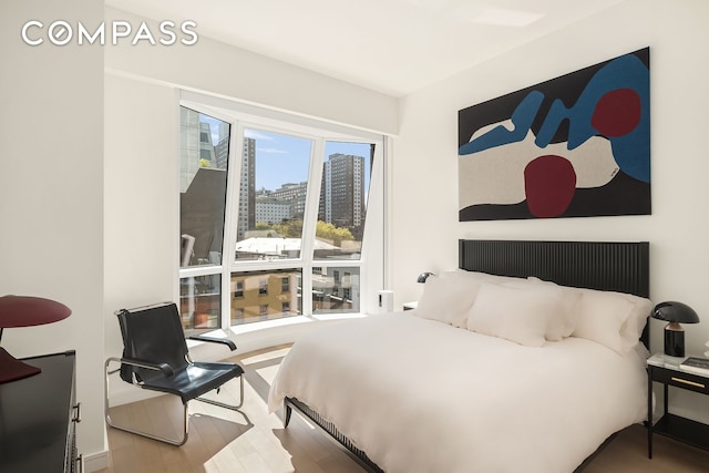 bedroom with a view of city and wood finished floors