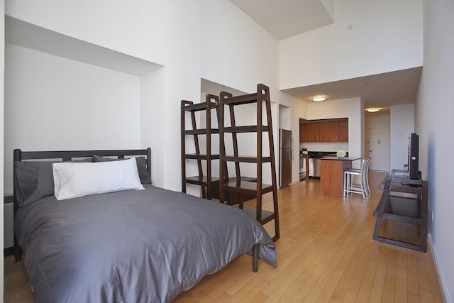 bedroom featuring light wood-style flooring, a high ceiling, and freestanding refrigerator