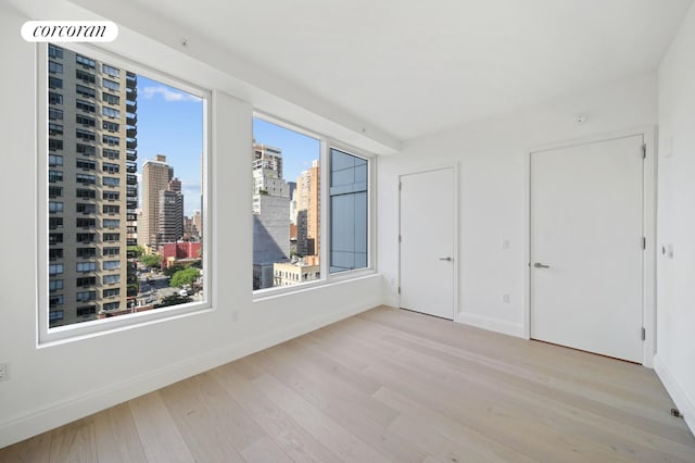 unfurnished room featuring baseboards, a view of city, and wood finished floors