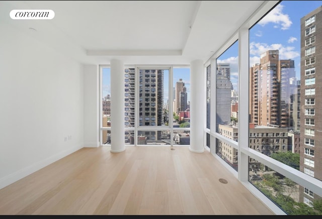 empty room featuring a city view, wood finished floors, visible vents, and floor to ceiling windows