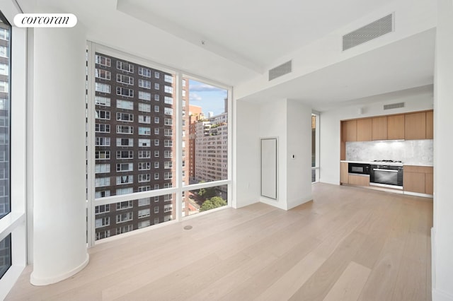 unfurnished living room featuring a city view, visible vents, light wood finished floors, and baseboards