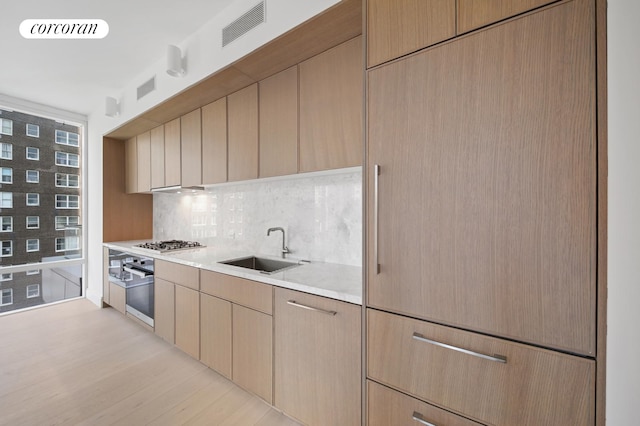 kitchen with visible vents, light wood-type flooring, a sink, light countertops, and tasteful backsplash