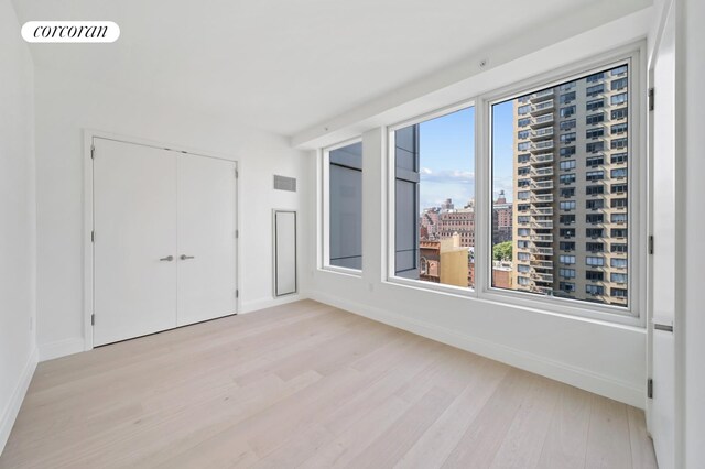 spare room with a view of city, visible vents, light wood-style flooring, and baseboards