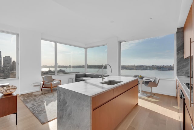 kitchen with modern cabinets, a kitchen island with sink, light wood-style flooring, a sink, and light countertops