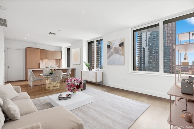 living room with visible vents, baseboards, light wood-style floors, and a city view