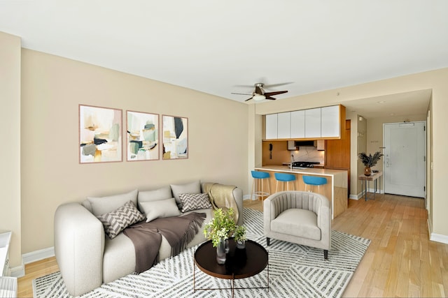 living room with ceiling fan, light wood-style flooring, and baseboards