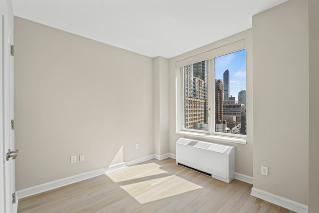 spare room with radiator, light wood-style flooring, a city view, and baseboards