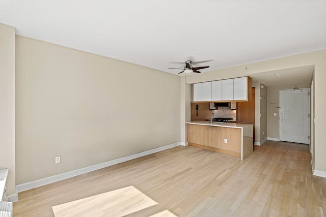 kitchen with tasteful backsplash, light wood-style floors, light countertops, a ceiling fan, and a peninsula