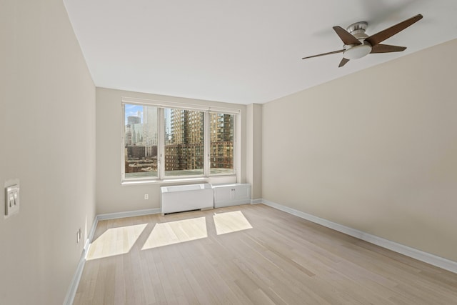 spare room featuring radiator, ceiling fan, baseboards, and light wood-style floors