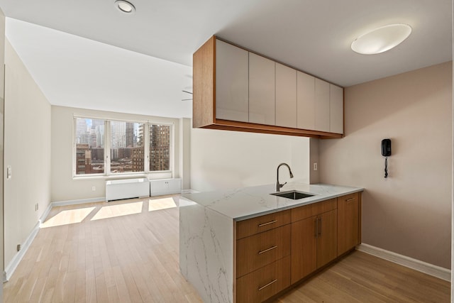 kitchen with light stone countertops, light wood-style floors, brown cabinets, a sink, and baseboards
