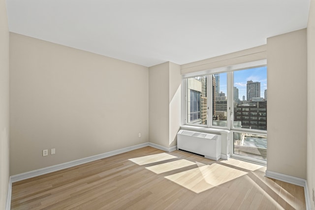 spare room with a view of city, baseboards, wood finished floors, and radiator