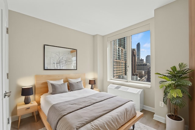 bedroom featuring radiator heating unit, wood finished floors, a view of city, and baseboards
