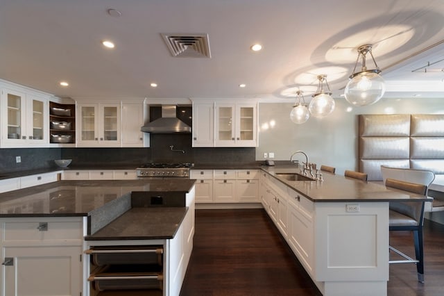 kitchen featuring a peninsula, a sink, dark countertops, wall chimney range hood, and range