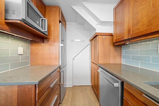 kitchen with light wood-style flooring, brown cabinets, backsplash, and stainless steel appliances