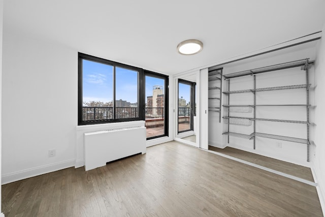 unfurnished room with baseboards, radiator, a city view, and wood finished floors