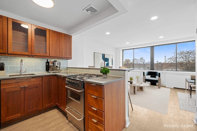 kitchen featuring visible vents, a peninsula, a sink, decorative backsplash, and stainless steel gas range oven