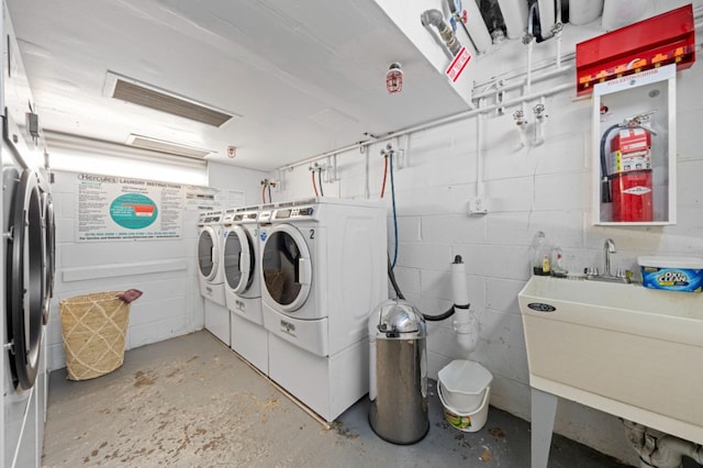 laundry room featuring washing machine and clothes dryer, visible vents, concrete block wall, and a sink