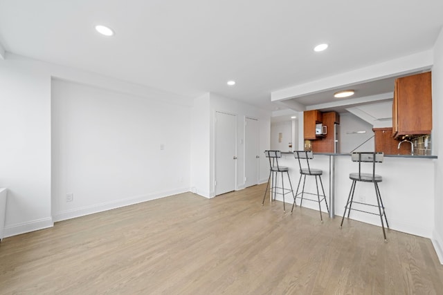 kitchen with dark countertops, a breakfast bar area, recessed lighting, brown cabinets, and light wood-style floors