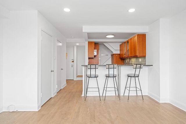 kitchen featuring a breakfast bar area, decorative backsplash, light wood-style flooring, recessed lighting, and brown cabinetry