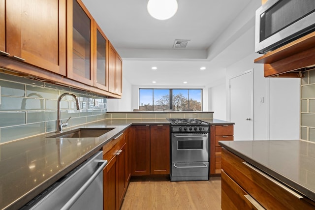 kitchen with light wood finished floors, a sink, stainless steel appliances, glass insert cabinets, and brown cabinets