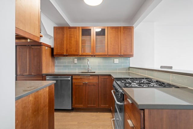 kitchen featuring a sink, stainless steel appliances, glass insert cabinets, tasteful backsplash, and light wood-type flooring