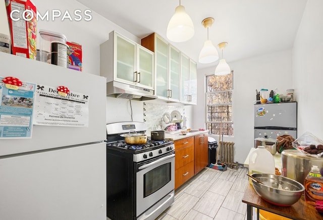 kitchen featuring radiator, under cabinet range hood, decorative light fixtures, brown cabinets, and stainless steel appliances