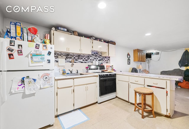 kitchen featuring gas stove, a peninsula, freestanding refrigerator, a sink, and light countertops