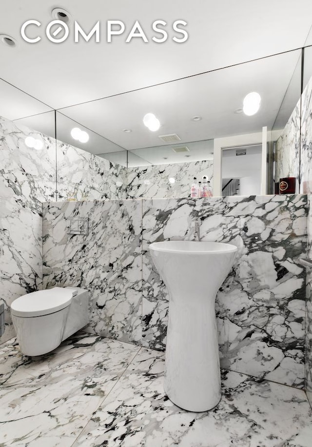 bathroom with stone wall, toilet, and marble finish floor