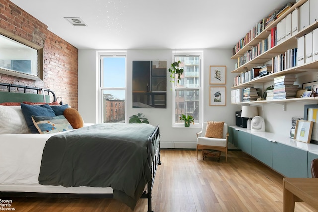 bedroom featuring light wood finished floors and brick wall