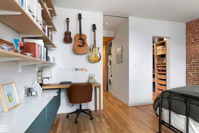 office area with light wood finished floors, brick wall, baseboards, and stacked washer and clothes dryer