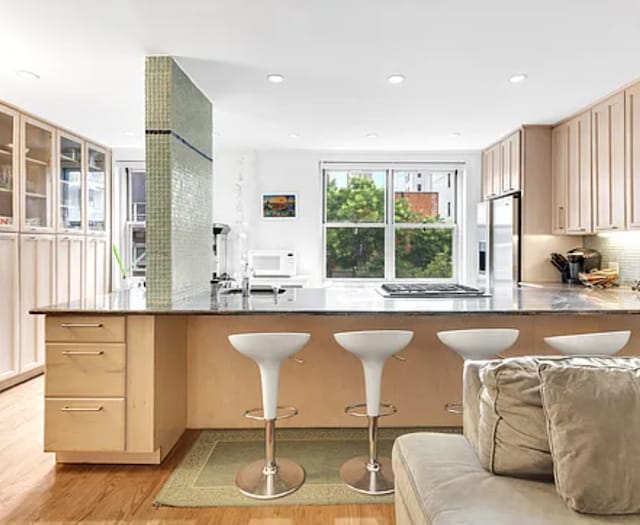 kitchen featuring light brown cabinets, a peninsula, a sink, stainless steel appliances, and light wood-style floors